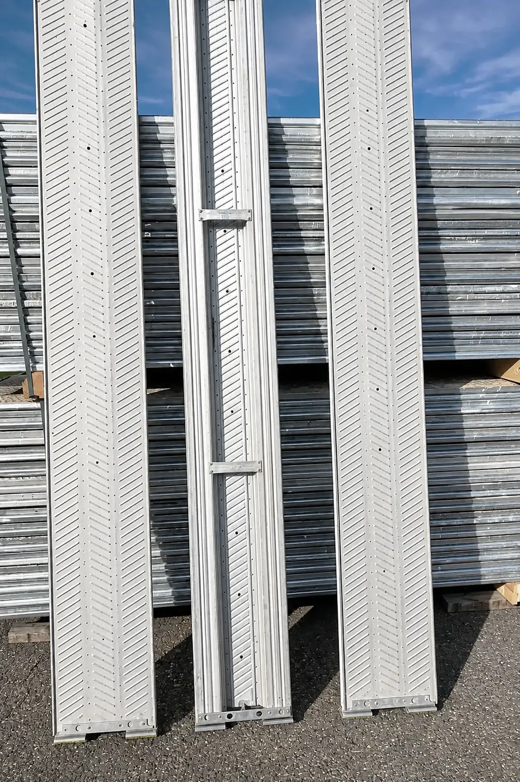 Drei Aluminium-Gerüstbeläge im Detail, dahinter Stapel verzinkter Rahmen